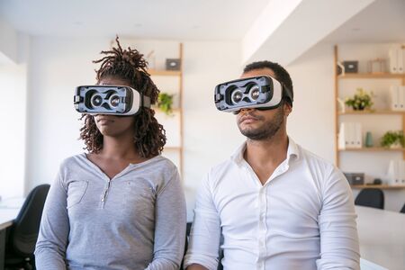 Diverse colleagues testing VR goggles. Young man and woman wearing virtual reality headset, sitting...