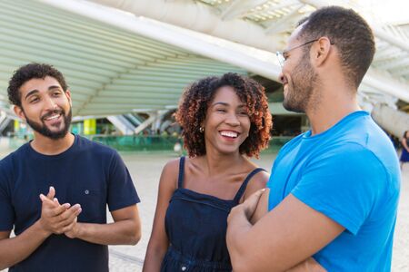 Multiethnic group of friends meeting outside and having fun. Diverse men and women standing at city...