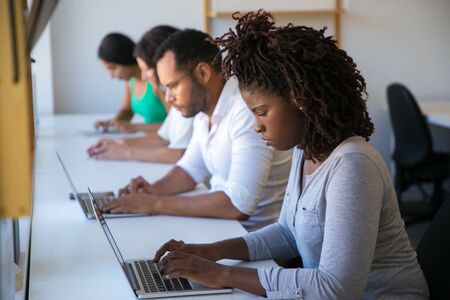 Team of developers testing software on digital devices. Man and women sitting at long desk, using laptops and tablets, looking at screen. Software conceptの写真素材