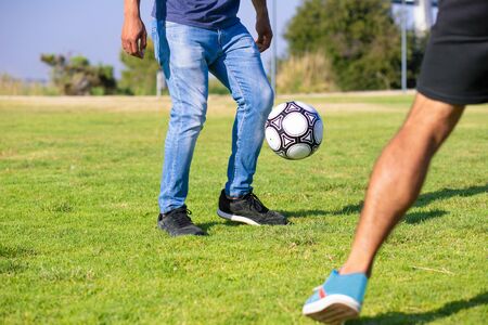 People playing soccer in park. Legs of man in casual jeans kicking football ball on grass. Outdoor activity conceptの写真素材