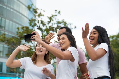 Group of cheerful young people posing for selfie. Smiling friends waving to camera phone. Concept of self portraitの写真素材