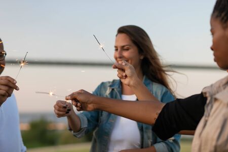 Closeup shot of young people with bengal lights in hands. Group of friends having fun at outdoor party. Concept of celebrationの写真素材
