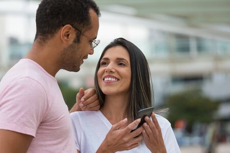 Smiling young couple looking at each other. Cheerful multiracial friends standing on street with...
