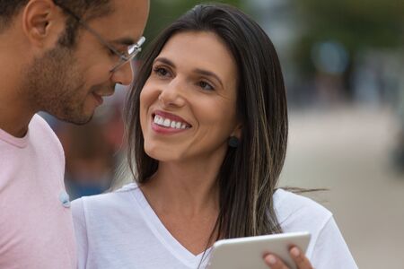 Smiling good friends with tablet on street. Cheerful multiracial couple using tablet. Communication and technology conceptの写真素材