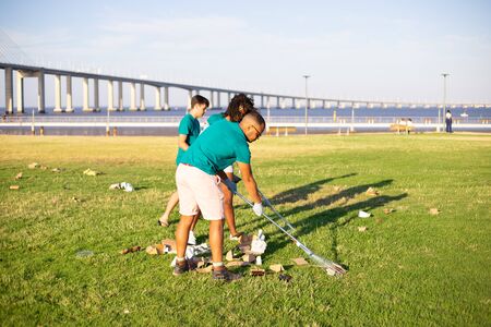 Group eco friendly activists cleaning city lawns near river. Young men and woman gathering rubbish with rakes on grass. Nature care conceptの写真素材