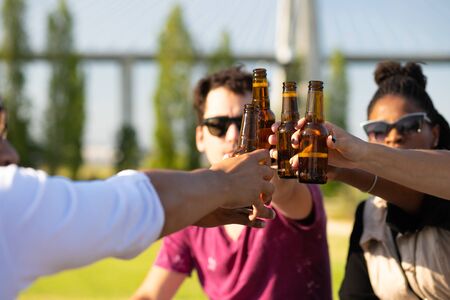 Informal multiethnic group of people drinking beer outdoors. Hands of young men and women holding bottles and toasting. Celebration conceptの写真素材