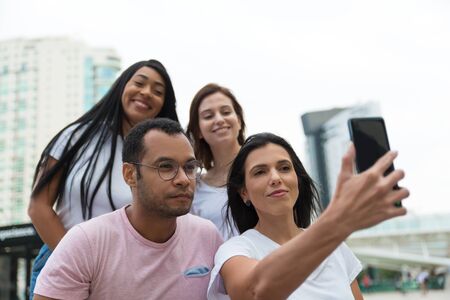 Group of friends taking selfie with smartphone on street. Cheerful young people posing for self...
