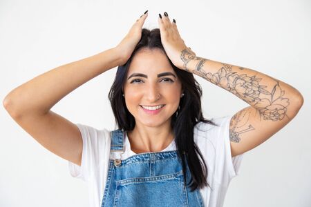 Smiling young brunette holding hands on head. Cheerful woman posing on white background. Female beauty conceptの写真素材