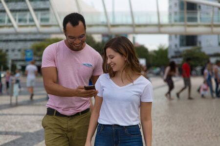 Smiling young couple looking at smartphone. Cheerful people talking and looking at phone during...