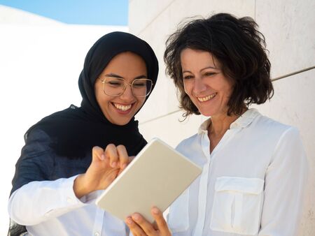 Happy business colleagues watching content on tablet screen together. Muslin employee using tablet...