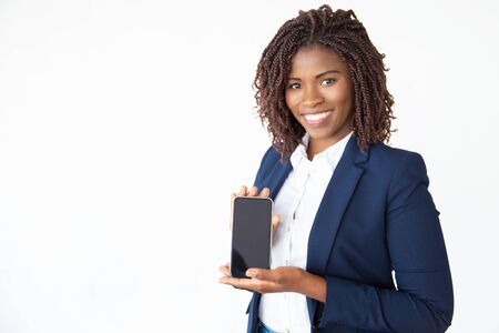 Happy successful businesswoman showing blank phone screen, advertising mobile app or software. Young African American business woman standing isolated over white background. Advertising conceptの写真素材