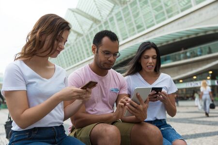 Group of young people using devices on street. Calm friends sitting with smartphones and tablet. Technology conceptの写真素材