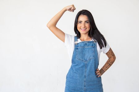 Smiling strong woman with raised hand. Cheerful young lady showing muscles. Girl power conceptの写真素材