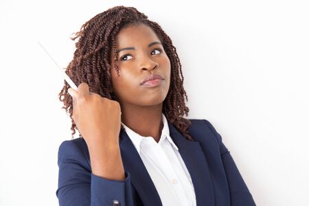 Pensive female student holding pen, looking away. Young African American business woman standing isolated over white background. Thinking over idea conceptの写真素材