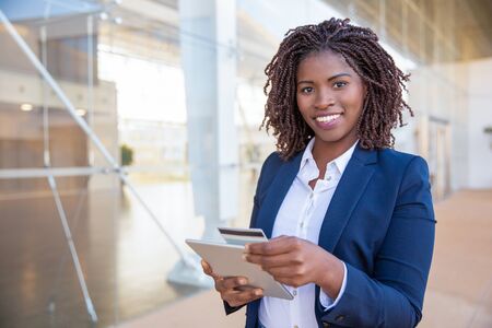 Happy cheerful customer paying online. Young African American business woman standing outside, using...