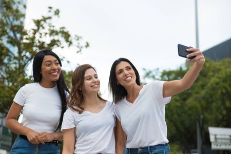 Joyful women posing for selfie on street. Cheerful young ladies taking selfie with smartphone. Concept of self portraitの写真素材