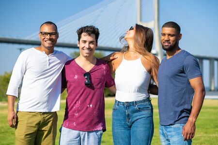 Happy team of friends posing outside. Line of young men and woman standing on grass, hugging each...