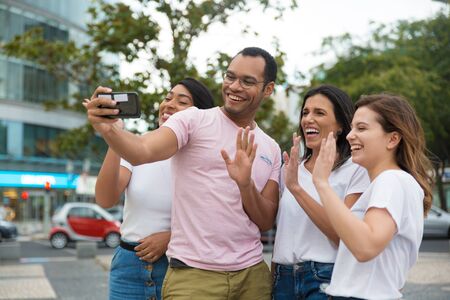 Smiling friends waving to camera phone. Group of cheerful young people posing for selfie. Concept of self portraitの写真素材
