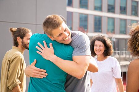 Multiethnic friends greeting each other. Happy young men and women smiling and hugging on street. Friendship conceptの写真素材