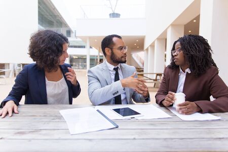 Multiethnic business colleagues discussing documents in cafe. Business man and women sitting at...