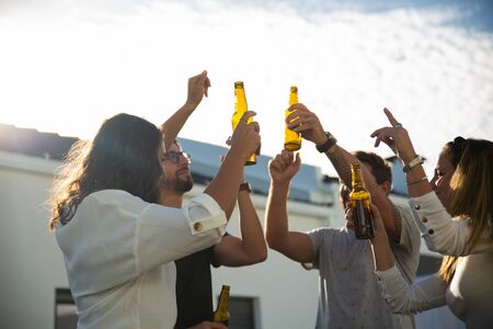 Group of friends dancing, toasting beer and celebrating great event on outdoor terrace. Young men and women in casual meeting outside. Communication and having fun conceptの写真素材