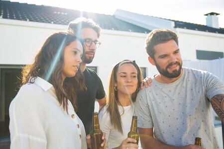 Group of friends taking selfie while drinking beer on outdoor terrace. Young men and women in casual...