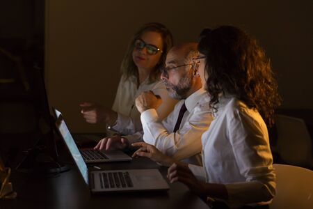 Business team working in dark office. Side view of professional businessman and businesswomen working with computers in dark office. Business and technology conceptの写真素材