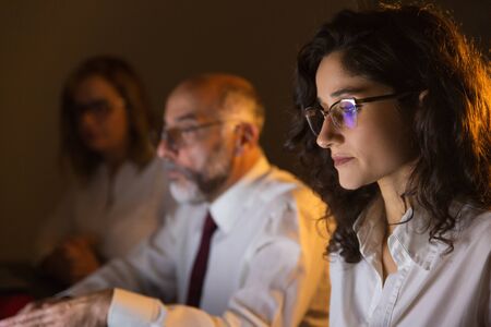 Tired business people working late. Side view of overworked businessman and businesswomen working in dark office. Business conceptの写真素材