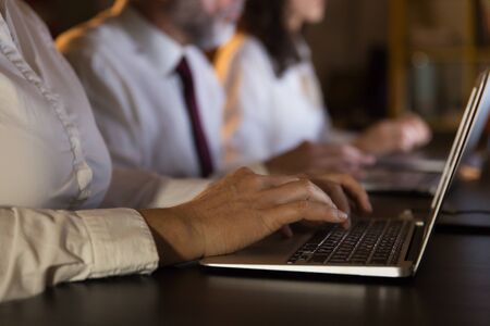 Partial view of business people using laptops. Cropped shot of male and female business colleagues working with laptop computers in dark office, close-up view. Business and technology conceptの写真素材