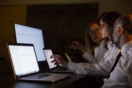 Business people discussing work in dark office. Professional male and female business colleagues looking at laptop computer screen and discussion project late at night. Business and technology conceptの写真素材