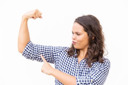 Funny strong Latin woman flexing and touching hand muscles. Young woman in casual checked shirt...