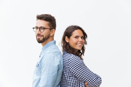 Happy positive couple standing back-to-back, looking at camera, smiling. Young woman in casual and man in glasses in glasses posing isolated over white background. Happy couple conceptの写真素材