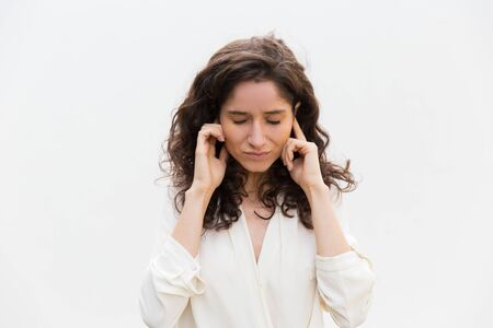 Stressed woman with closed eyes plugging ears with fingers. Wavy haired young woman in casual shirt standing isolated over white background. Conflict or stress conceptの写真素材