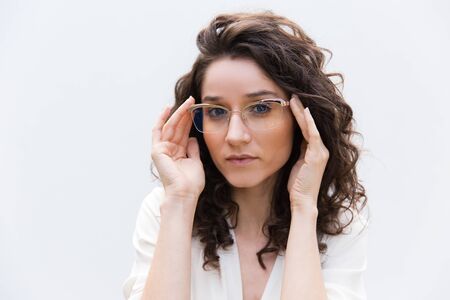 Portrait of serious positive female professional in glasses. Wavy haired young woman in casual shirt...