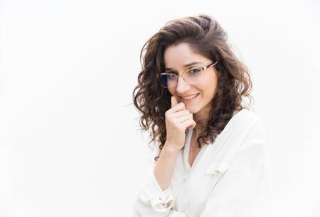 Pensive smiling female professional in glasses leaning chin on hand. Wavy haired young woman in...