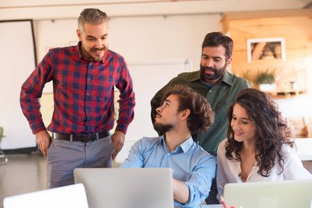 Creative workgroup discussing project ideas, looking at laptop screen. Business colleagues in casual sitting together in contemporary office space. Teamwork or brainstorming conceptの写真素材
