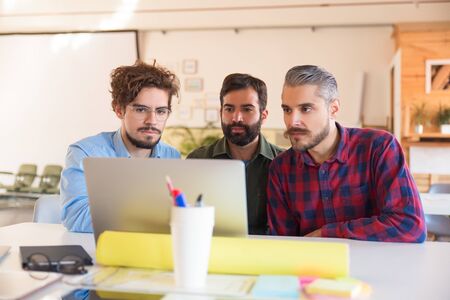 Serious creative team watching video content on monitor. Business colleagues in casual working together in contemporary office space. Internet communication conceptの写真素材
