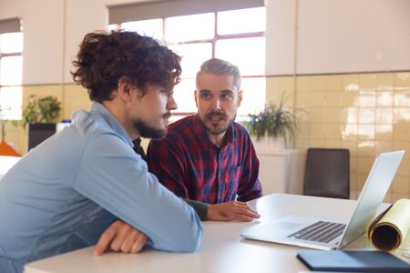 Male coworkers watching content on monitor and discussing project. Business colleagues in casual working together in contemporary office space. Teamwork conceptの写真素材