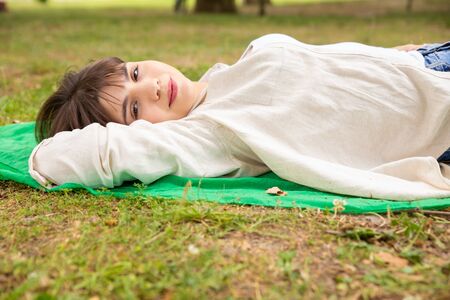 Young woman lying on meadow in park. Side view of beautiful young woman lying in green grass and...