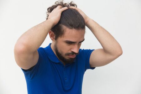 Sad frustrated guy holding head with both hands, feeling depressed. Handsome bearded young man in blue casual t-shirt posing isolated over white background. Depression or problem conceptの写真素材