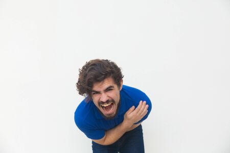 Frustrated unhappy guy screaming with pain, holding stomach, bending. Handsome bearded young man in blue casual t-shirt posing isolated over white background. Bellyache conceptの写真素材