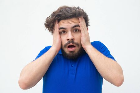 Forgetful shocked guy holding head, suddenly remembering something important. Handsome bearded young man in blue casual t-shirt posing isolated over white background. Failure conceptの写真素材