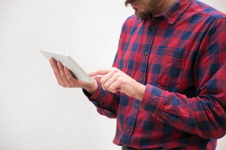 Cropped shot of man using digital tablet. Close-up partial view of man in checkered shirt using tablet computer on grey background. Wireless technology conceptの写真素材