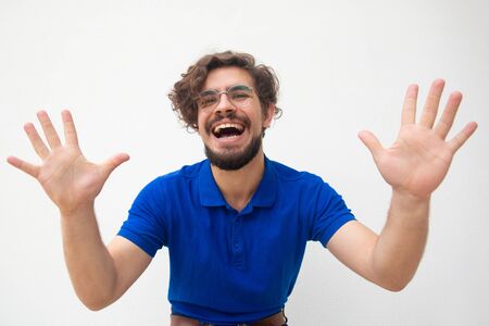 Excited joyful crazy guy touching air, showing palms, laughing. Handsome bearded young man in blue casual t-shirt posing isolated over white background. Fun or joy conceptの写真素材