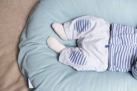 Legs and feet of baby lying on soft blue mattress, wearing grey pants and socks. Closeup of little child in home interior. Baby clothes conceptの写真素材