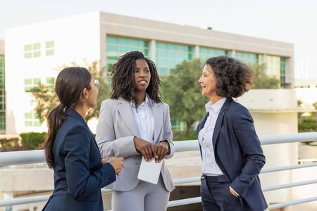 Positive excited colleagues chatting on office building terrace. Business women meeting and talking outside in city. Office friendship conceptの写真素材