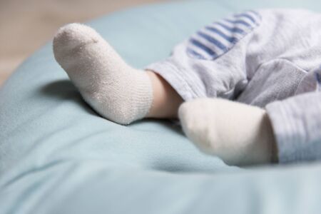 Tiny feet of baby lying on soft blue mattress, wearing socks. Closeup of little child in home interior. Baby clothes conceptの写真素材