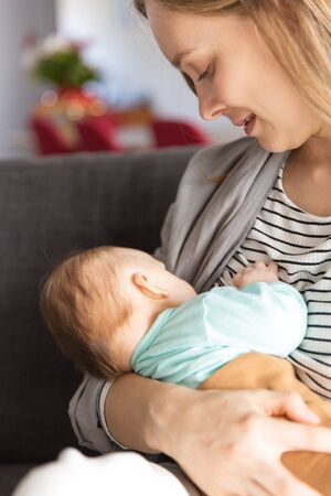 Focused positive new mother breastfeeding baby. Portrait of young woman and cute little child in...