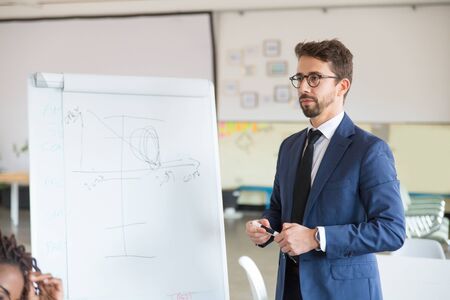 Business coach standing near whiteboard and looking at distance. Confident Caucasian manager doing presentation. Business training conceptの写真素材
