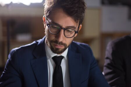 Closeup shot of focused man in eyeglasses working in office. Serious handsome businessman wearing...